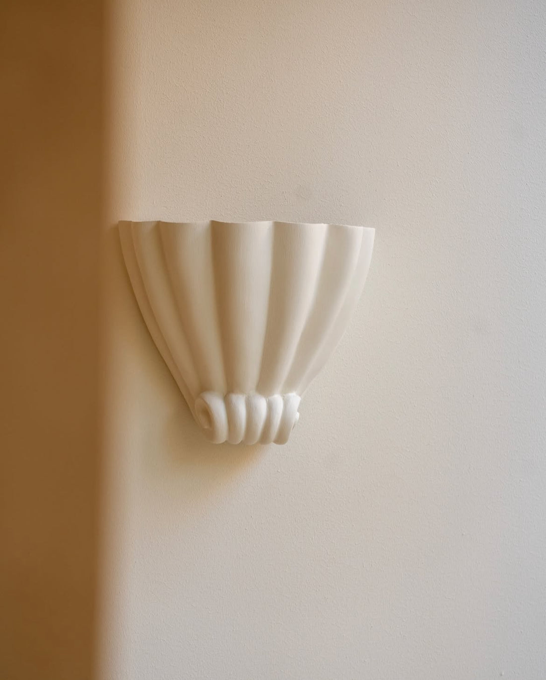 A white plaster scallop shell-shaped wall sconce on a light wall.