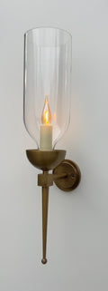 Brass wall sconce with an illuminated candle bulb and clear glass hurricane.