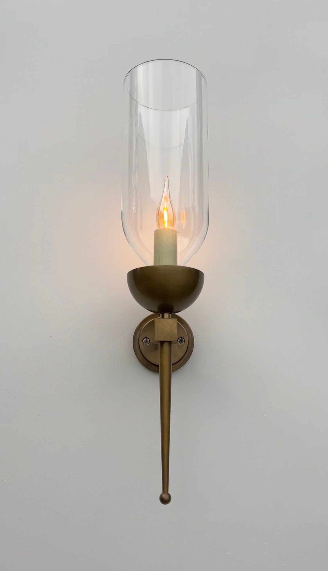Brass wall sconce with an illuminated candle bulb and clear glass hurricane.