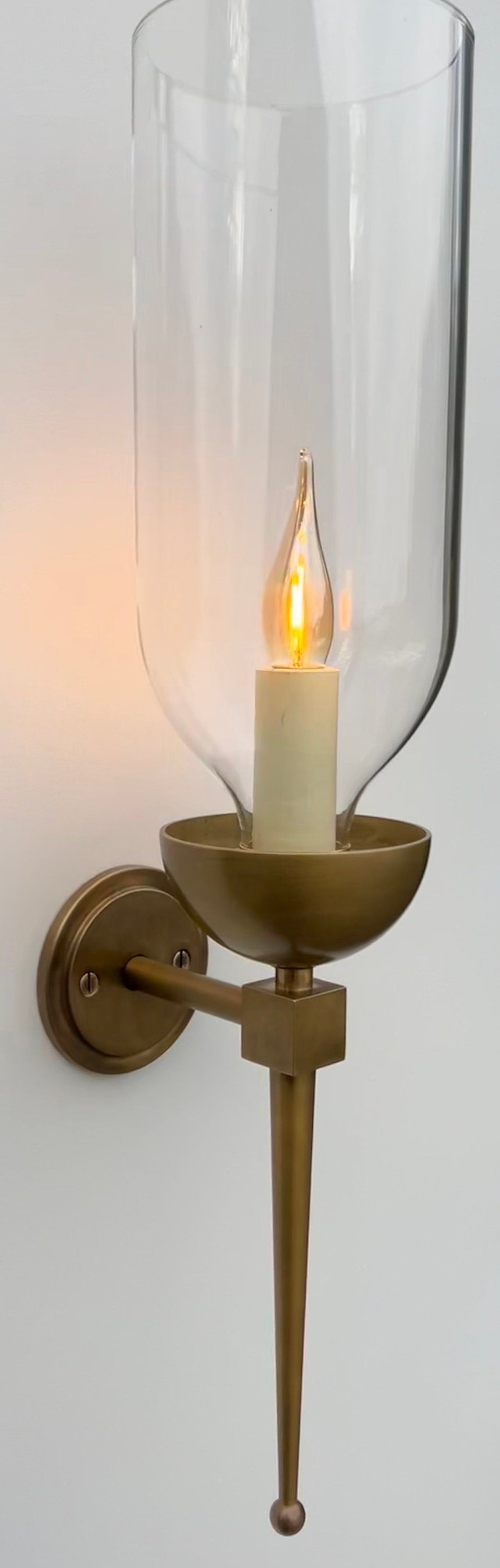 Brass wall sconce with an illuminated candle bulb and clear glass hurricane.