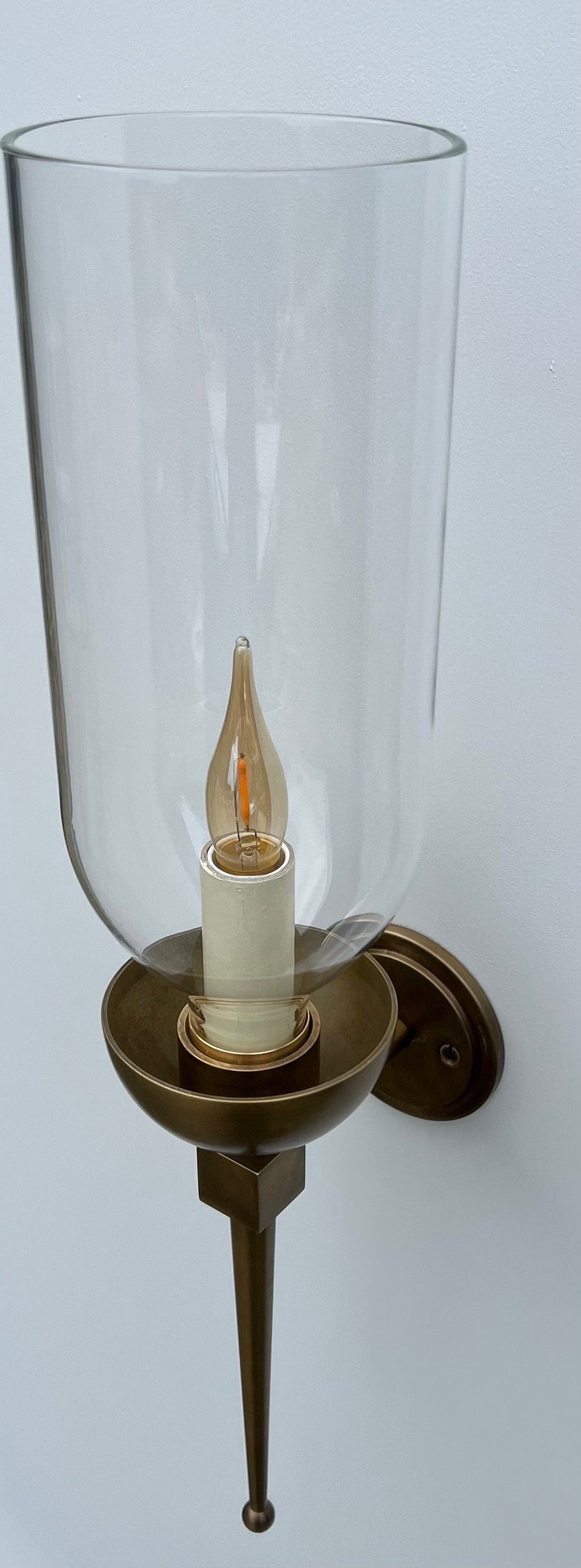 Brass wall sconce with an illuminated candle bulb and clear glass hurricane.