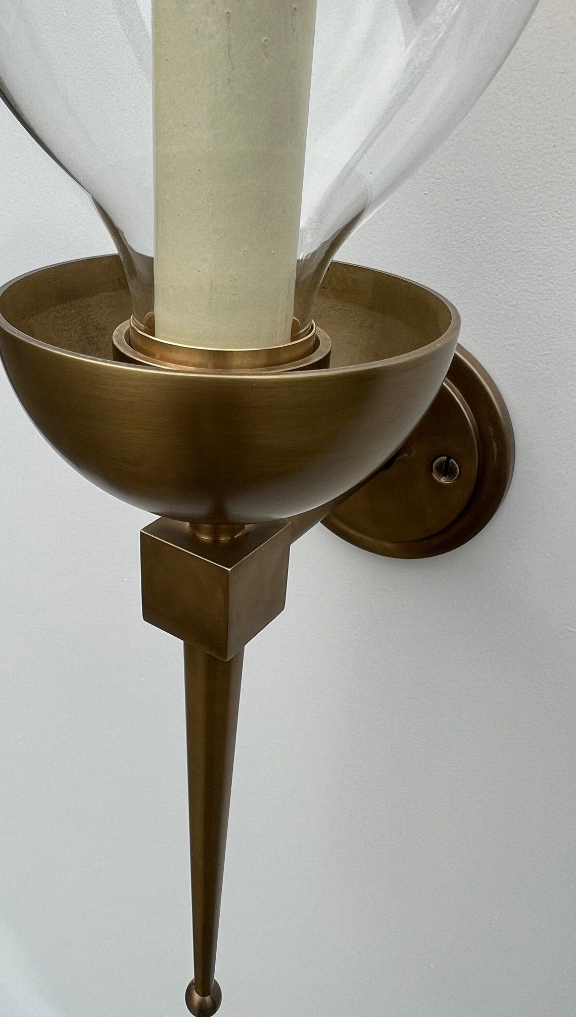 Close-up of a brass wall sconce with a candle bulb and glass shade.