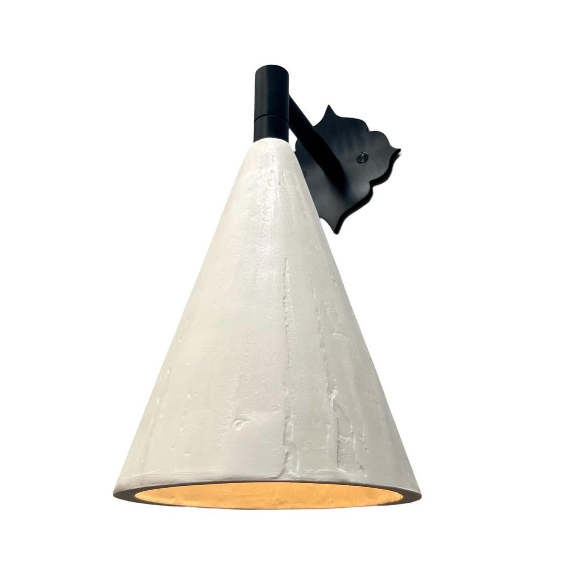 White conical wall sconce with a decorative black backplate, casting warm light.
