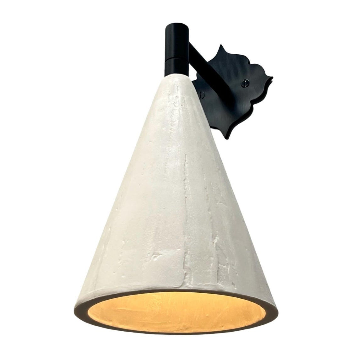 White conical wall sconce with a decorative black backplate, casting warm light.