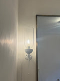 White wall sconce with clear glass hurricane and light bulb next to the bathroom mirror.