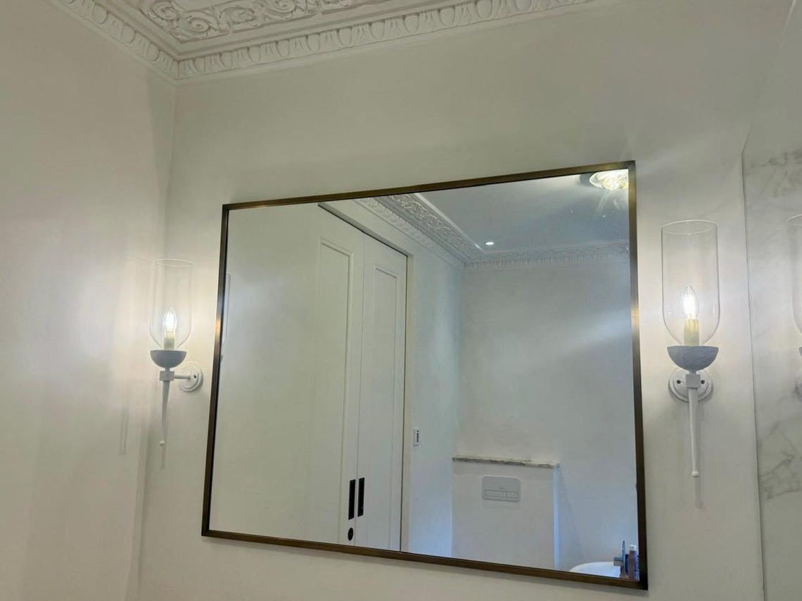 Bathroom with a large mirror flanked by two white wall sconces with clear glass.