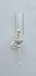 White wall sconce with clear glass and a flickering candle-style bulb.