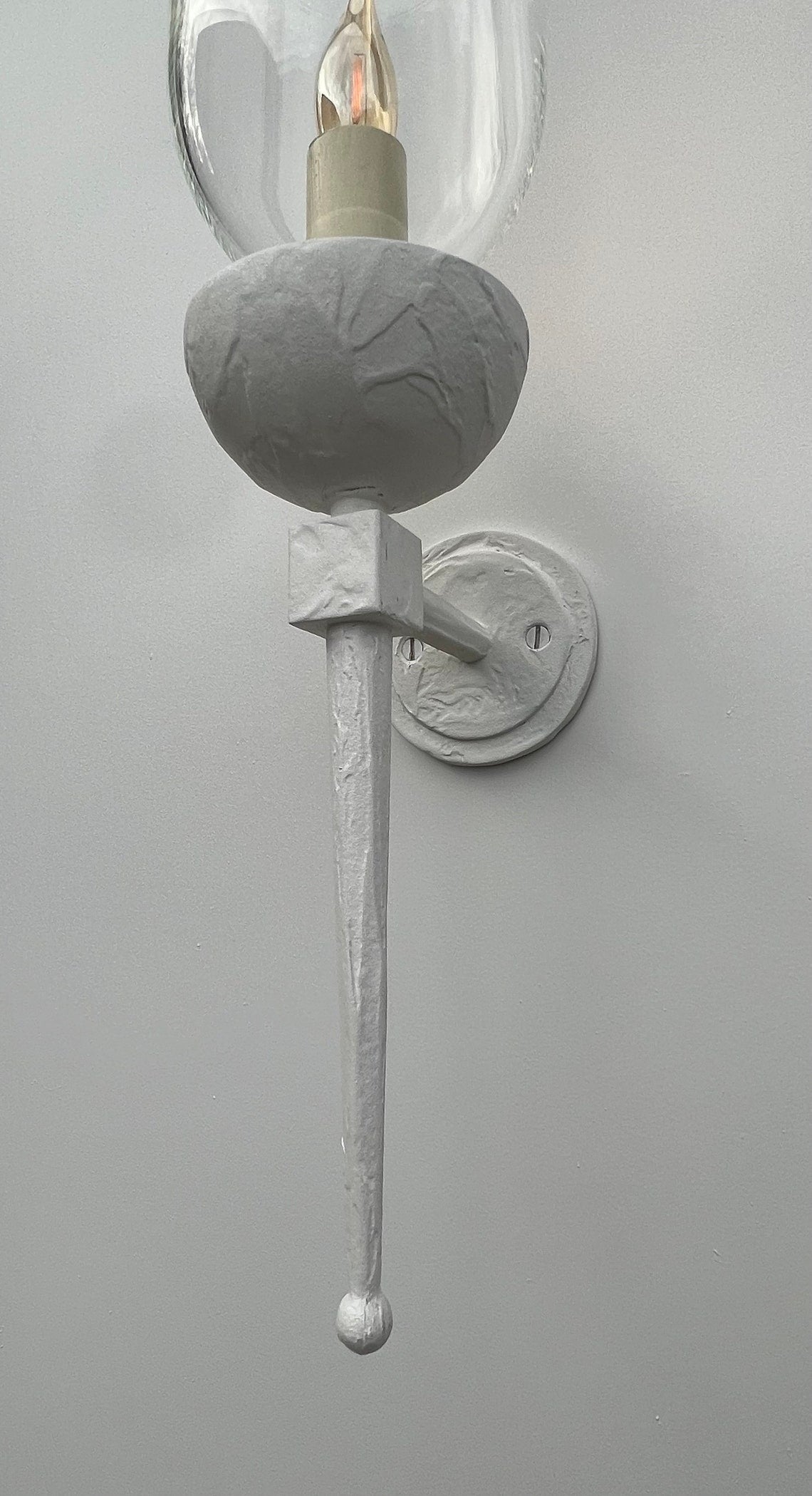 Close up of a white wall sconce with a torch design and clear glass shade.