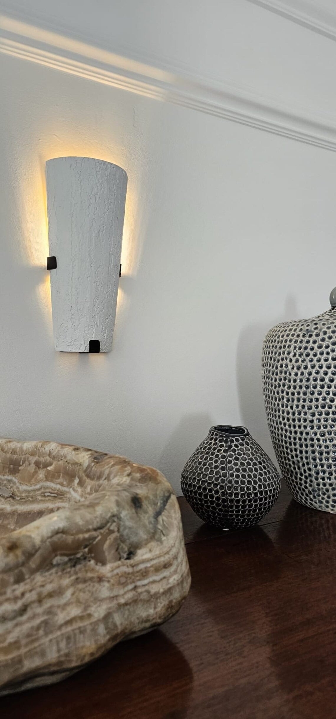 Wall sconce over wooden furniture with decorative vases.