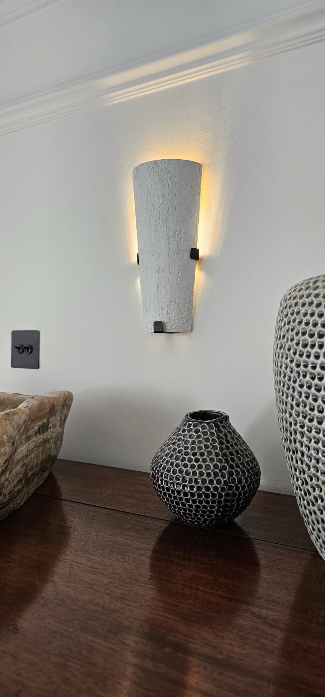Wall sconce over wooden furniture with decorative vases.