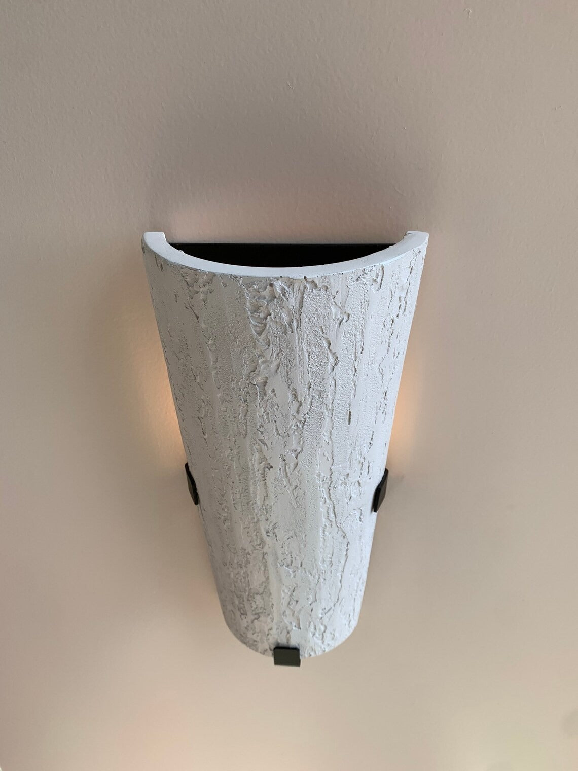 A tall, inverted cone-shaped wall sconce with a textured, bark-like white finish. It is mounted on a light-colored wall with three small black square brackets visible