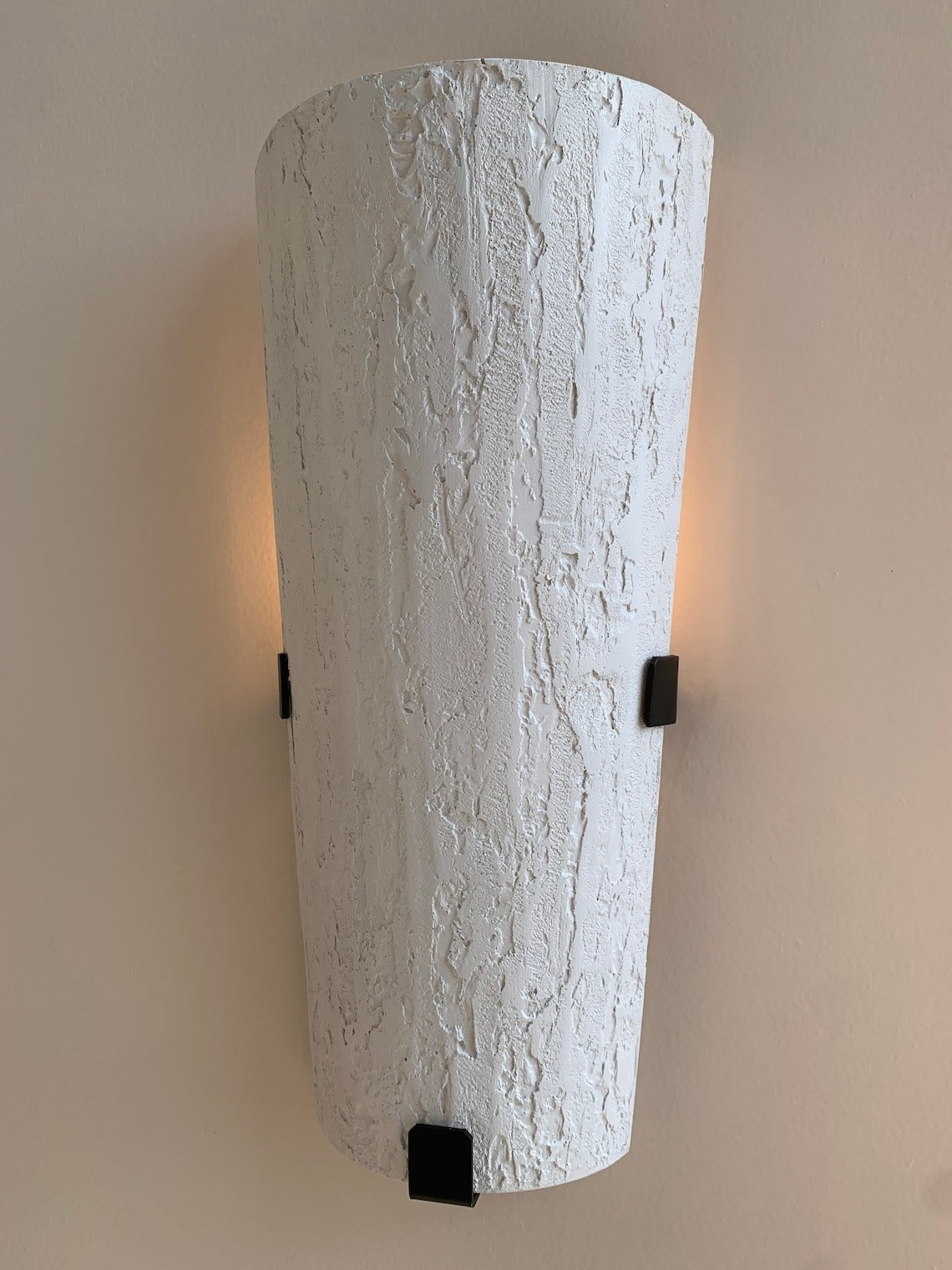 A tall, inverted cone-shaped wall sconce with a textured, bark-like white finish. It is mounted on a light-colored wall with three small black square brackets visible.