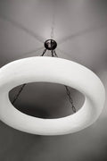 A white, textured circular chandelier hangs from a dark ceiling plate by chains.