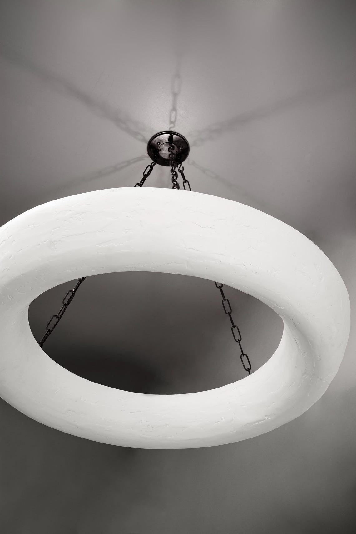 A white, textured circular chandelier hangs from a dark ceiling plate by chains.