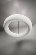  A modern, off-white, textured circular chandelier is suspended from a dark, round ceiling plate by four dark metal chains. The light fixture casts subtle shadows on the plain gray ceiling above.