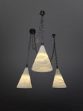 Three pendant lights with textured, translucent white conical glass shades hang at varying heights from a dark ceiling. Each light is suspended by a dark metal chain, and the shades are illuminated from within, showcasing their swirled or rippled patterns against a dark gray background.