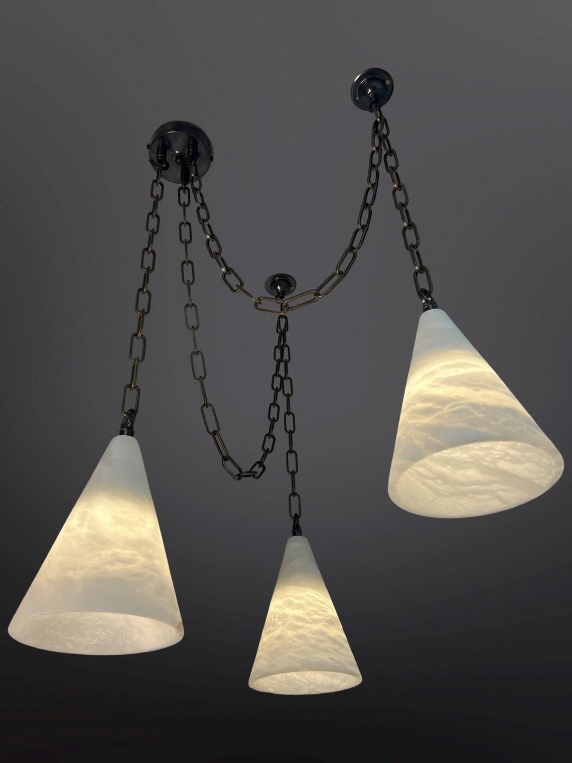 Three conical glass pendant lights with dark chains against a dark background.