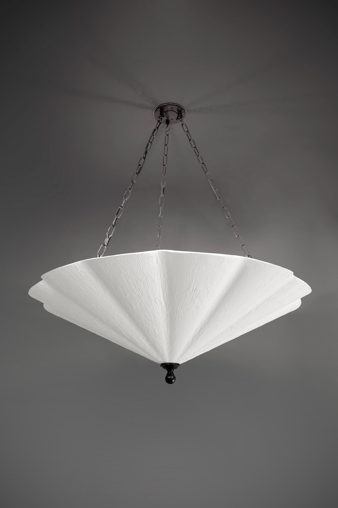A large, white fluted chandelier hangs from a dark ceiling plate by chains.