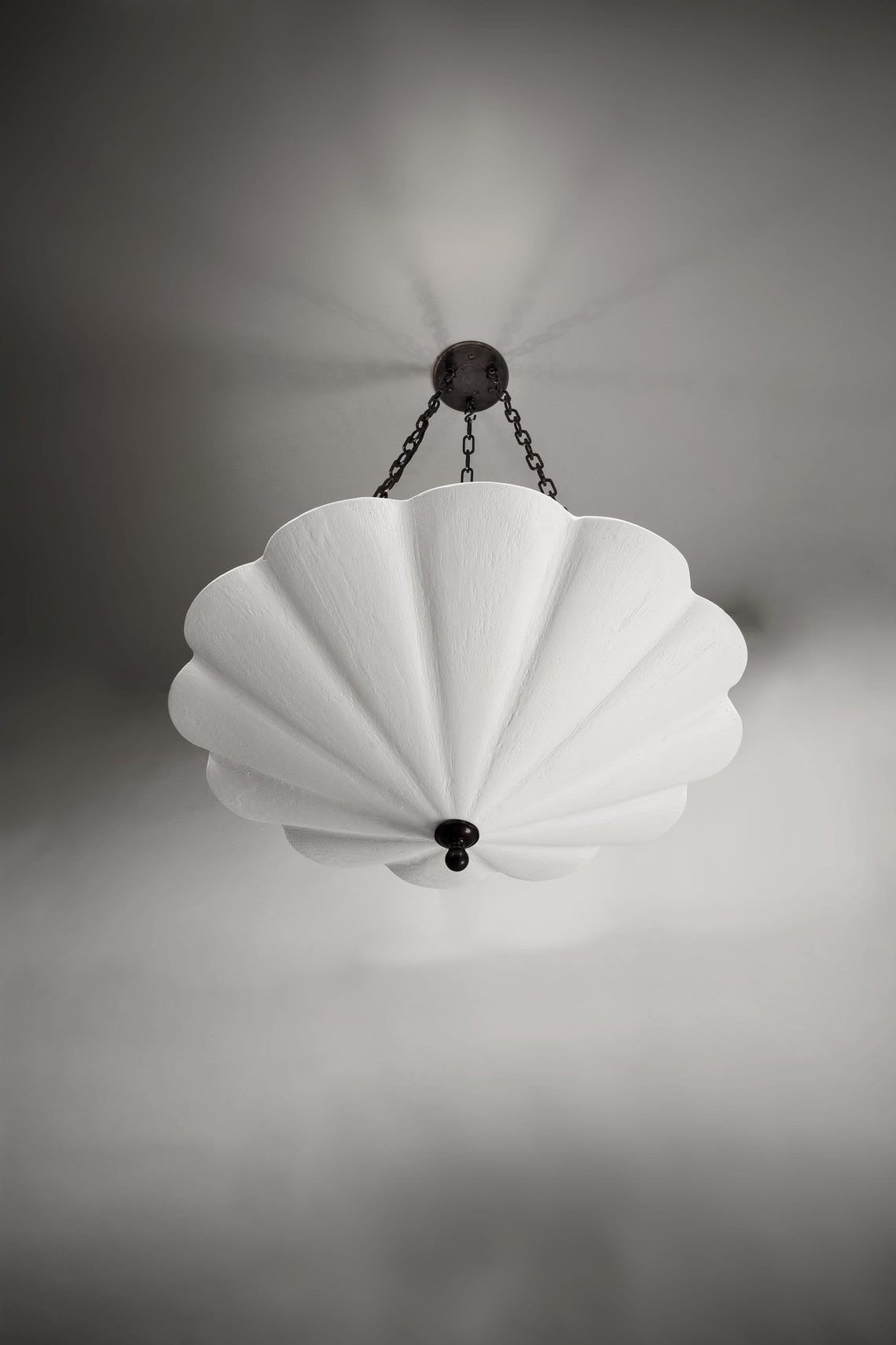 The Small Fluted Pendant Plaster Chandelier, featuring a white, fan-like or fluted plaster shade, suspended by dark metal chains from a matching ceiling mount.