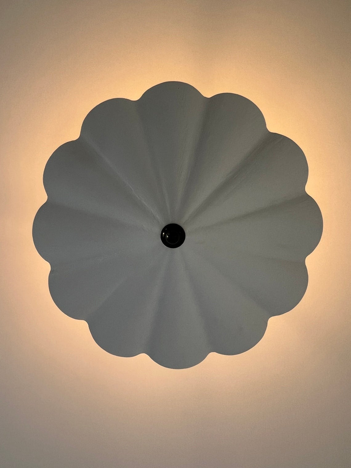 A white, scalloped ceiling light with a dark center, viewed from below.