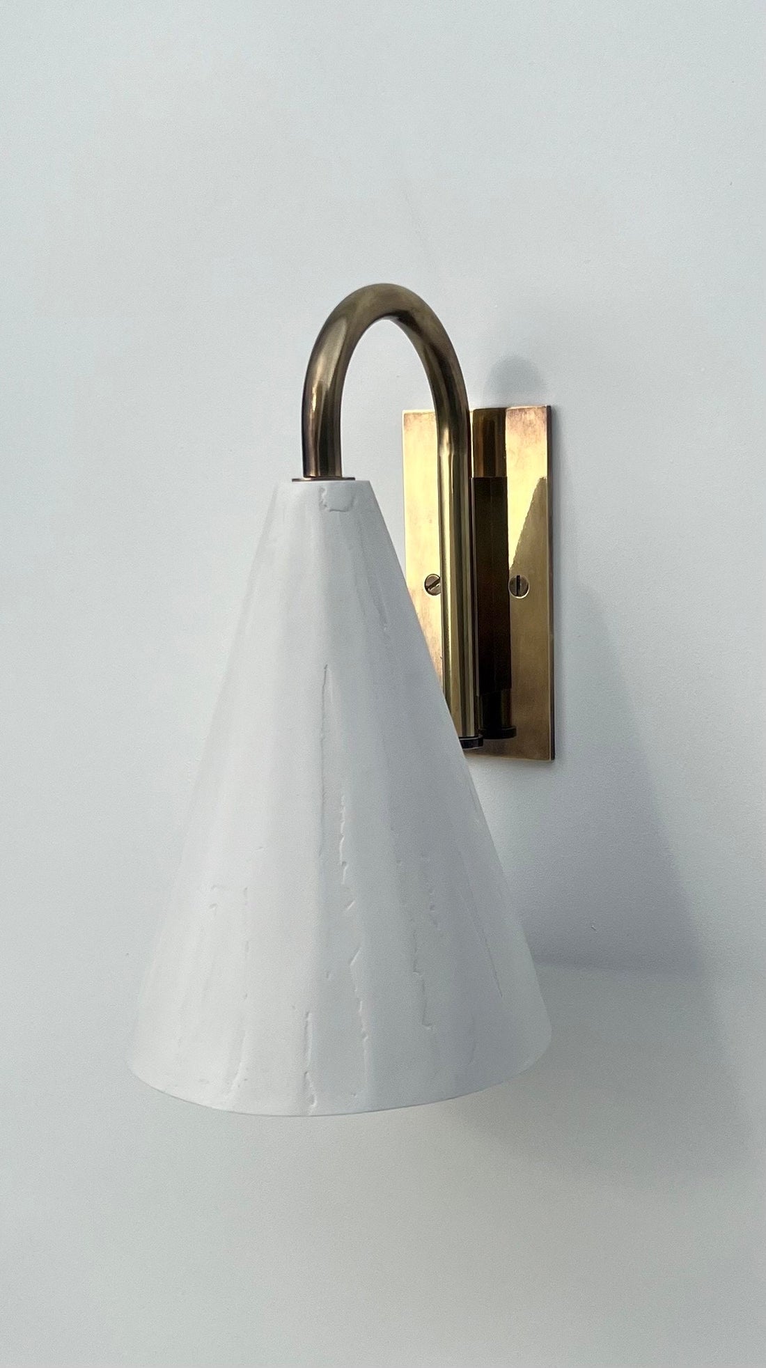A close-up of a white conical wall light with a brass swan neck arm.