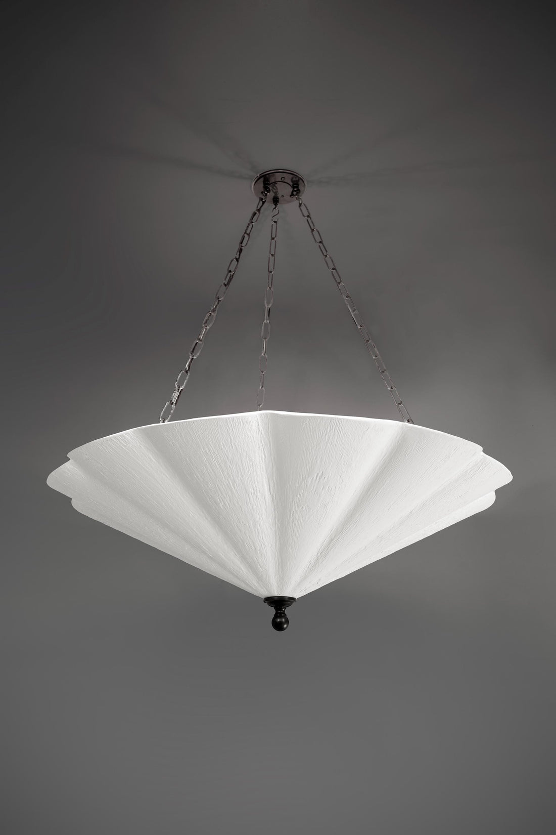 A large, white fluted chandelier hangs from a dark ceiling plate by chains.
