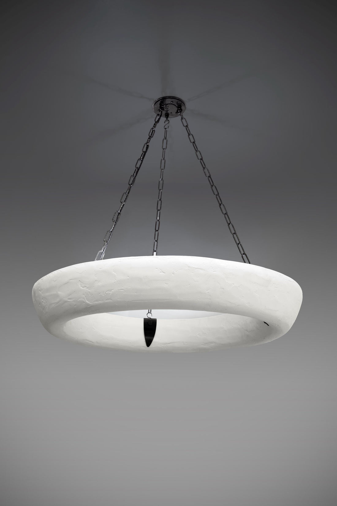 A white, textured circular chandelier with a dark pendant, suspended from chains against a grey ceiling.