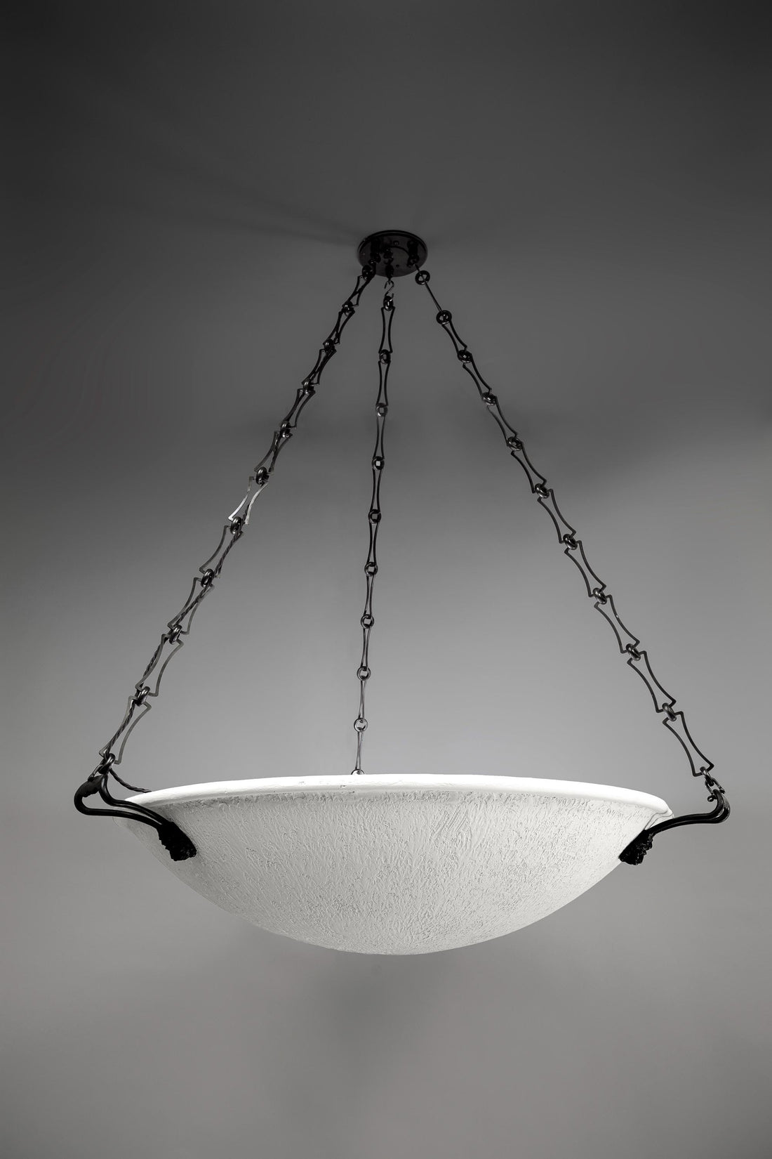 The Lion's Mane Chandelier, a Neo-Classical design, features a wide, textured white bowl-shaped diffuser suspended by three elaborate dark bronze chains with decorative elongated links. The chains attach to the bowl via curved dark bronze brackets, and the fixture hangs from a matching ceiling mount.