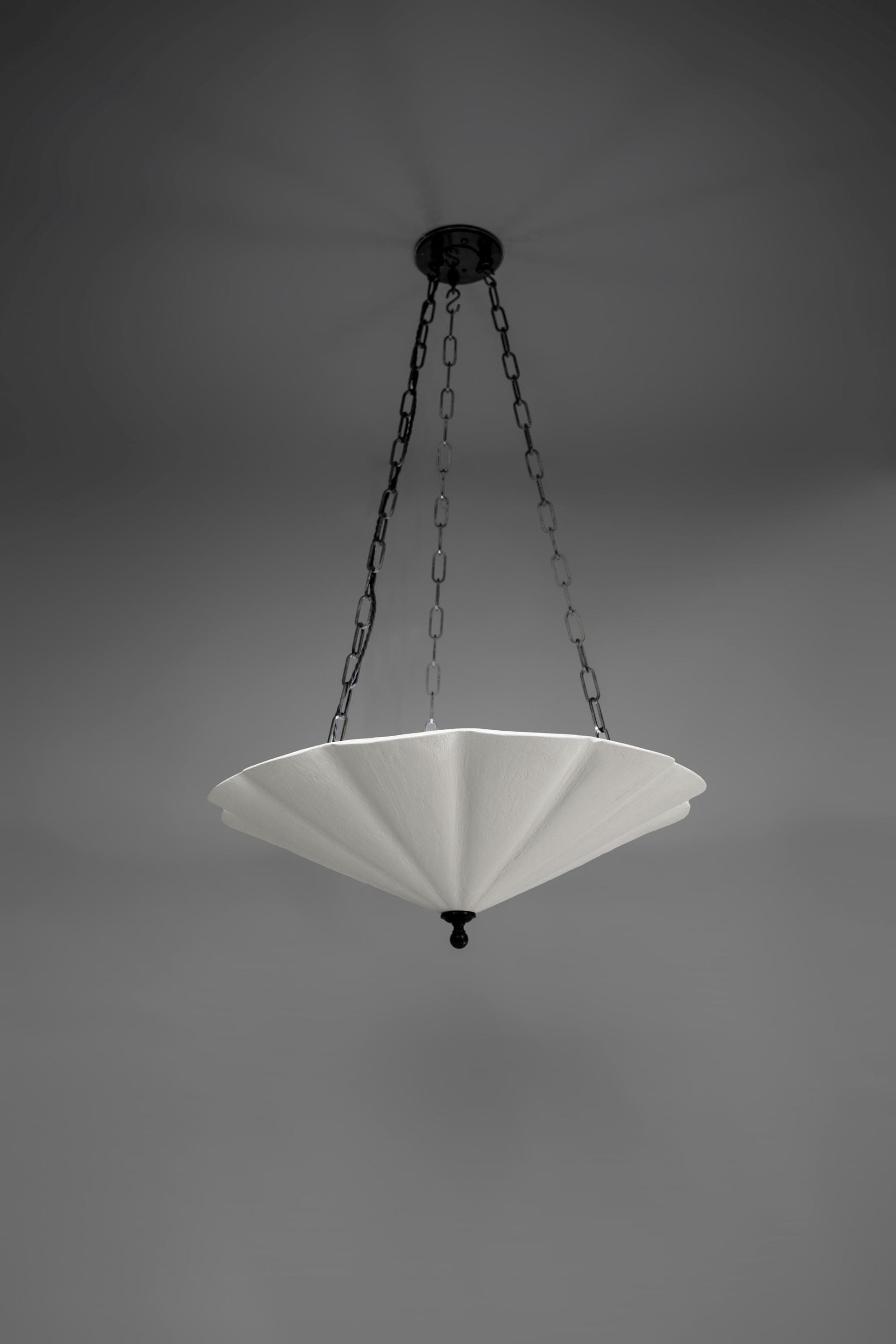 The Small Fluted Pendant Plaster Chandelier, featuring a white, fan-like or fluted plaster shade, suspended by dark metal chains from a matching ceiling mount.