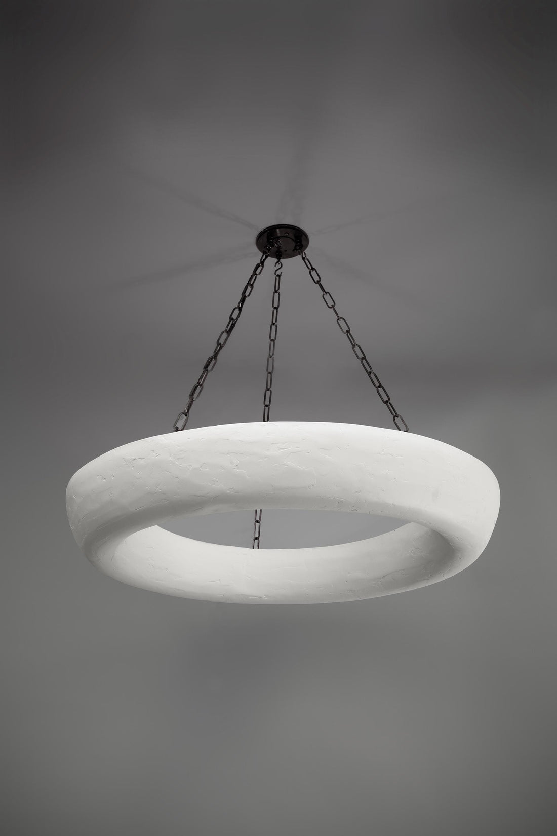A white, textured circular chandelier hangs from a dark ceiling plate by chains.