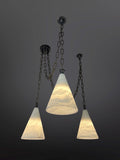 Three pendant lights with textured, translucent white conical glass shades hang at varying heights from a dark ceiling. Each light is suspended by a dark metal chain, and the shades are illuminated from within, showcasing their swirled or rippled patterns against a dark gray background.