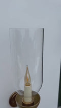 Brass wall sconce with an illuminated candle bulb and clear glass hurricane - detail video.