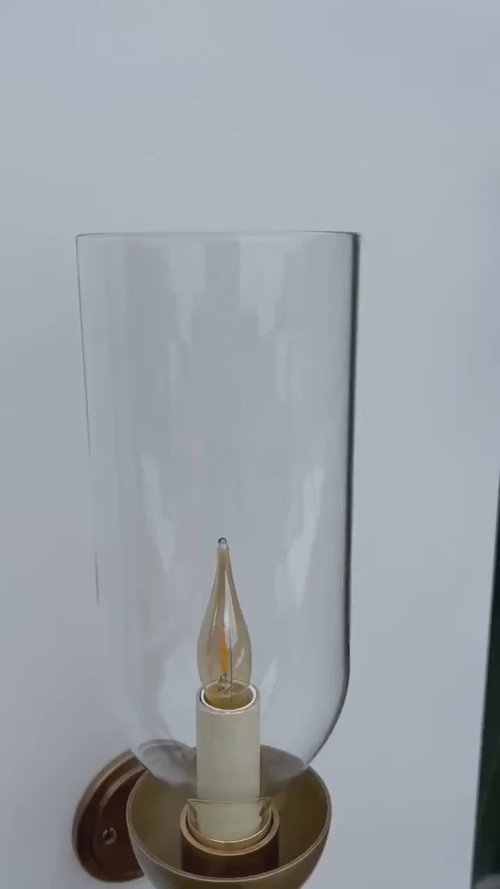 Brass wall sconce with an illuminated candle bulb and clear glass hurricane - detail video.